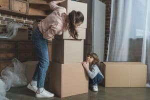 Mom packing while small daughter hunches at the foot of the boxes looking up